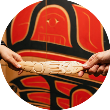 Two hands, Indigenous artwork, and feathering carving.
