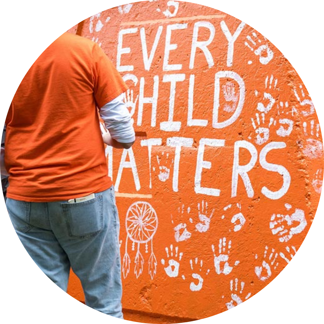 person shown from the back wearing an orange shirt, pictured in front of a painted artwork that reads Every Child Matters in painted lettering on an orange background
