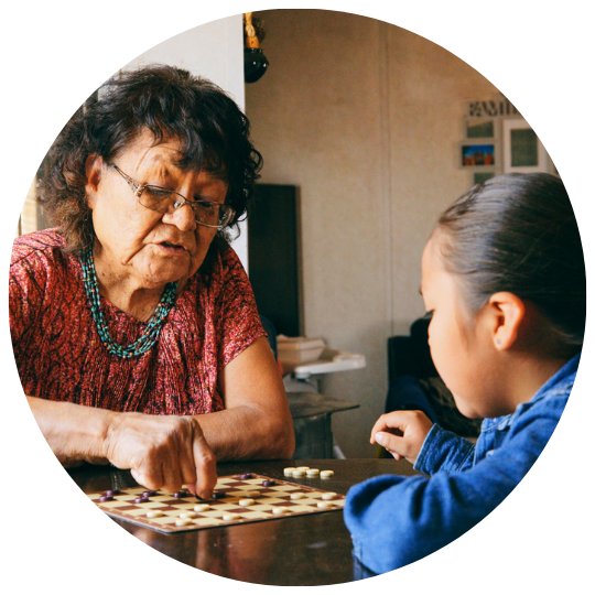 Indigenous elder playing a game at a kitchen table with a young indigenous girl