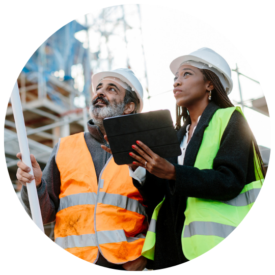 Construction workers observing a building they are working on, that is under construction. They wear high-vis vests