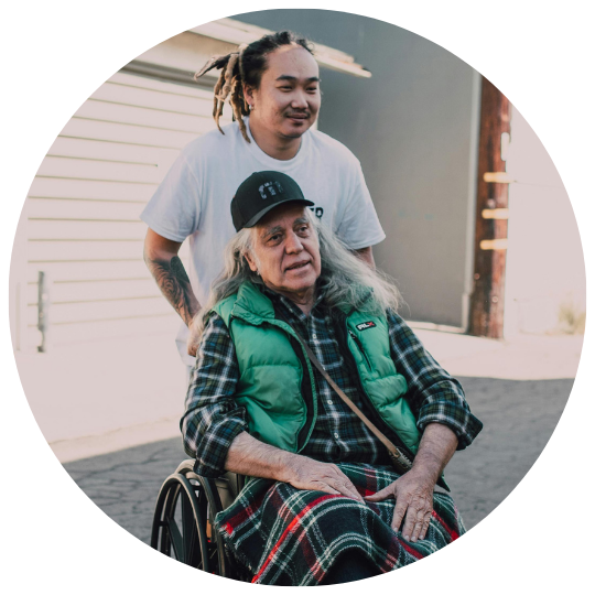 Young man pushing elderly man in wheelchair on the street