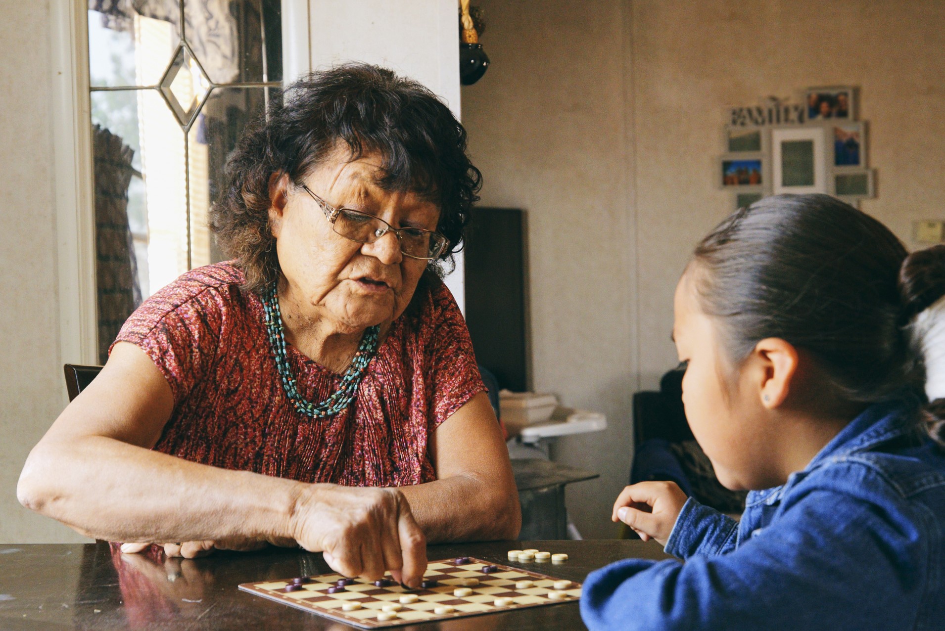 Indigenous elder and young indigenous child playing a game at a table in a kitchen