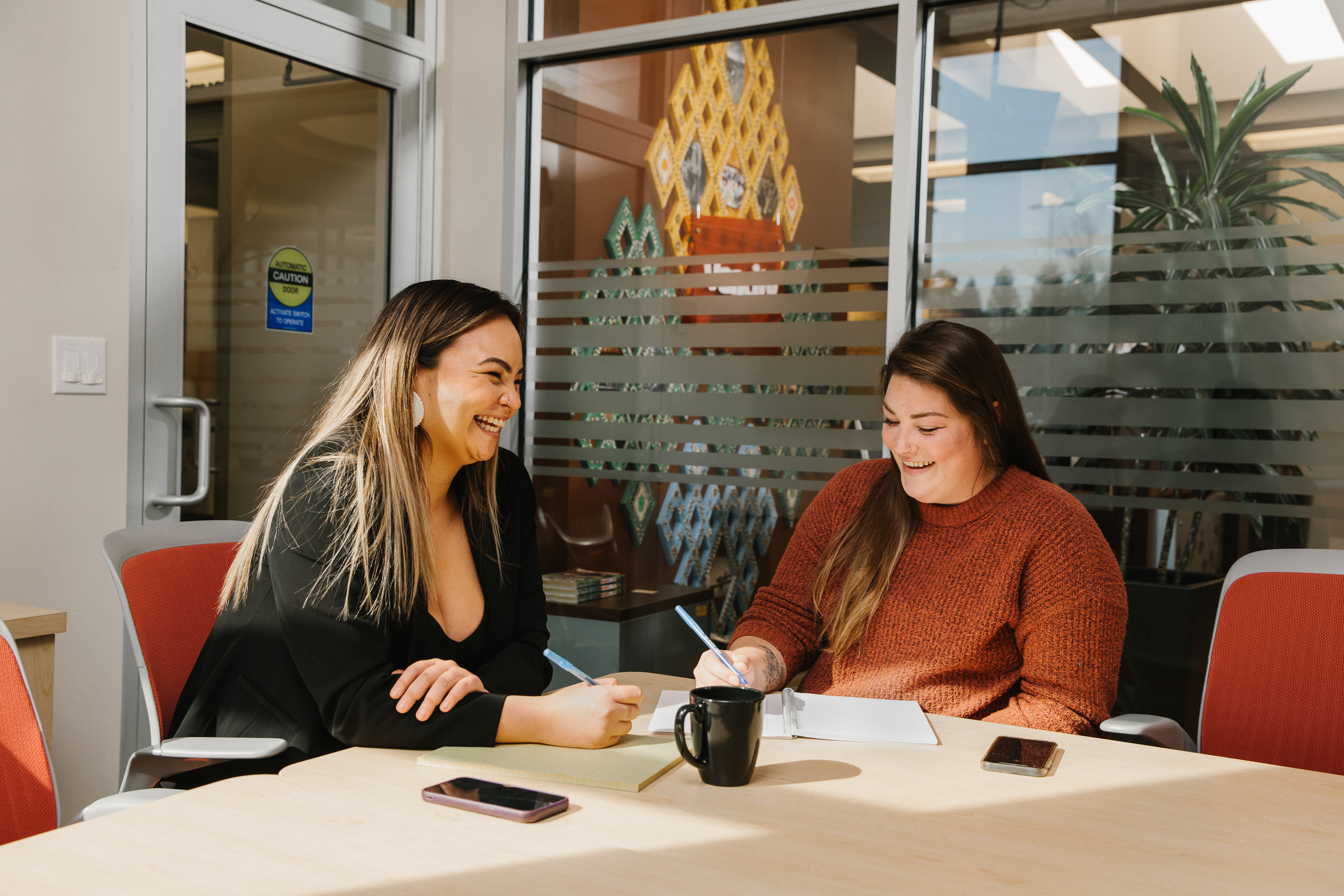 Two women sitting at desk in office room laughing