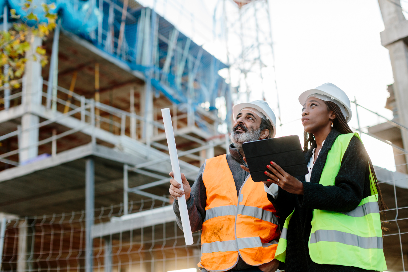 Construction workers looking up at a building that is under construction. They wear high-vis vests