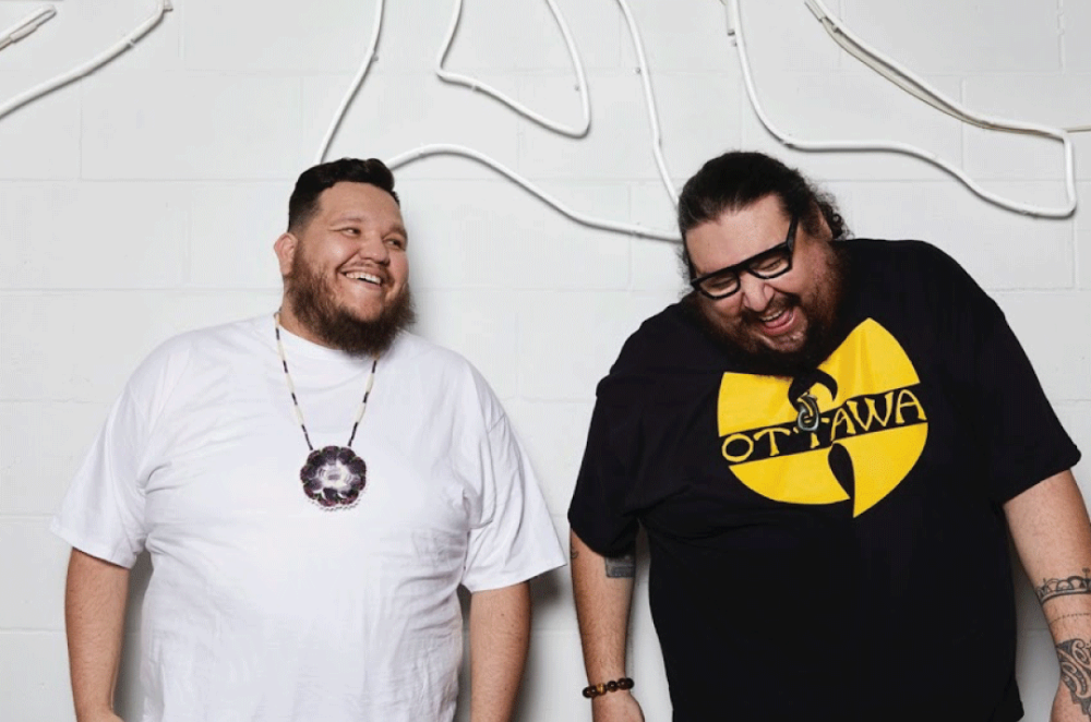 Image of the members of The Halluci Nation, Indigenous music artists. They are laughing together, standing in front of a white textured wall