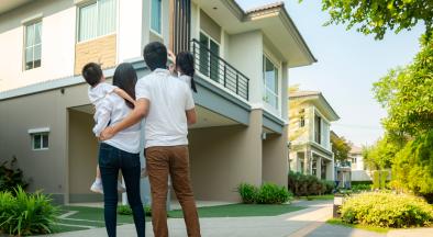 Family of two parents and two kids standing with their backs to the camera facing a house