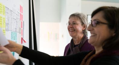 two women looking at a white board with sticky notes on it
