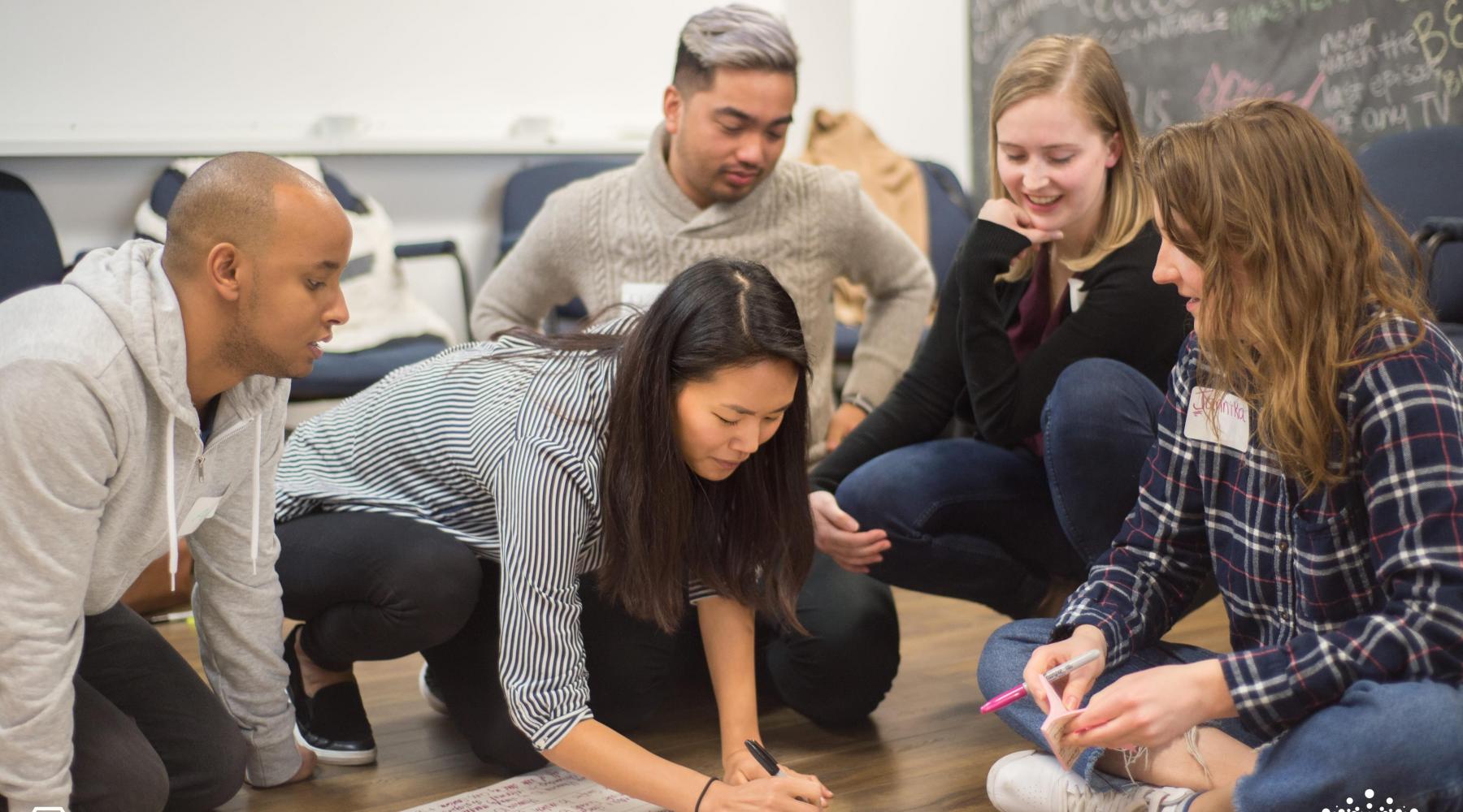 youth gathered around a table, writing on a piece of paper